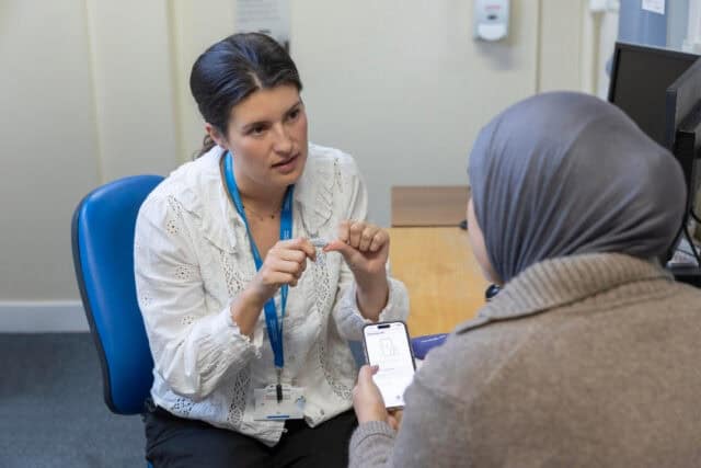 An audiologist sits with a patient and helps them with a hearing aids app.