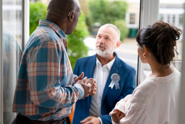 A political candidate talking to a man and a woman on the doorstep of their house