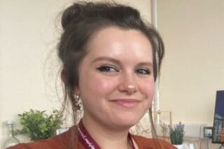 RNID storyteller, Caitlin, has brown hair tied up. She smiles at the camera.