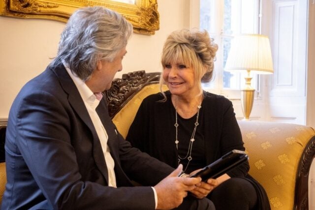 Dr Aamer Khan and Lesley Reynolds sit together on a sofa. They look at each other and are smiling.