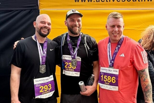 Three men stand together after running Taunton half marathon. They wear medals and are smiling.