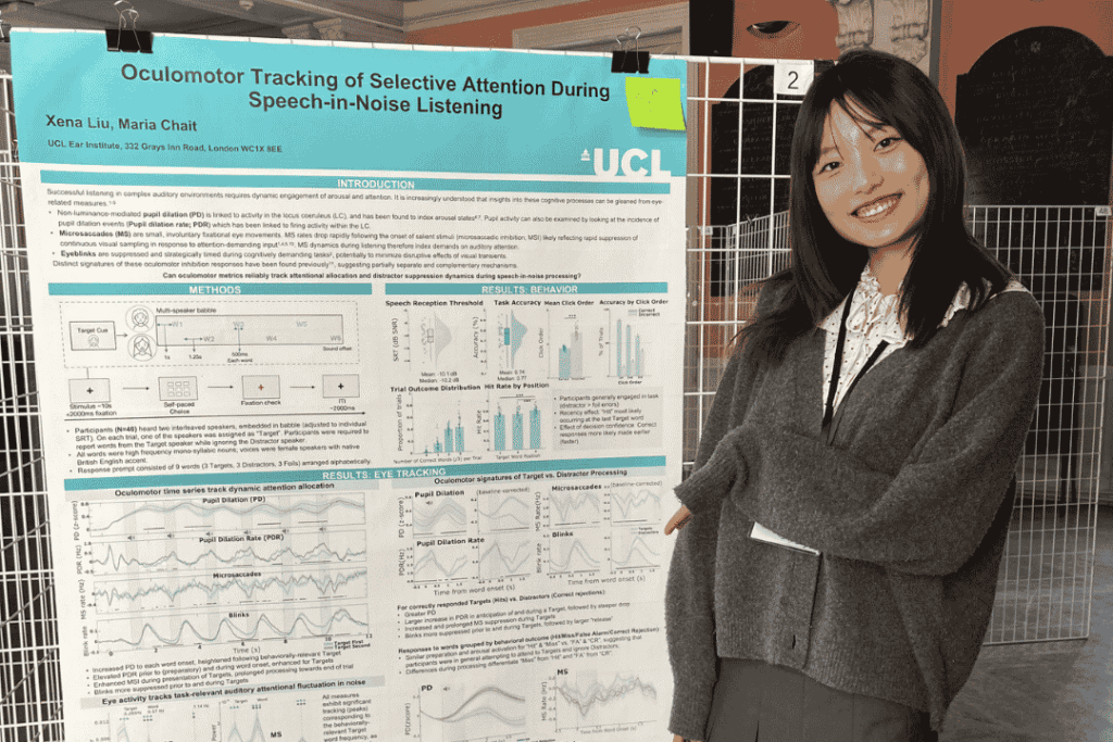 RNID researcher, Xena, stands beside a display showing research findings at the Speech in Noise workshop.