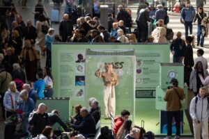 Tasha Ghouri smiling and signing inside a glass box at London's St Pancras International station