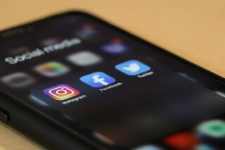 A phone lies on a table., The screen shows social media icons.