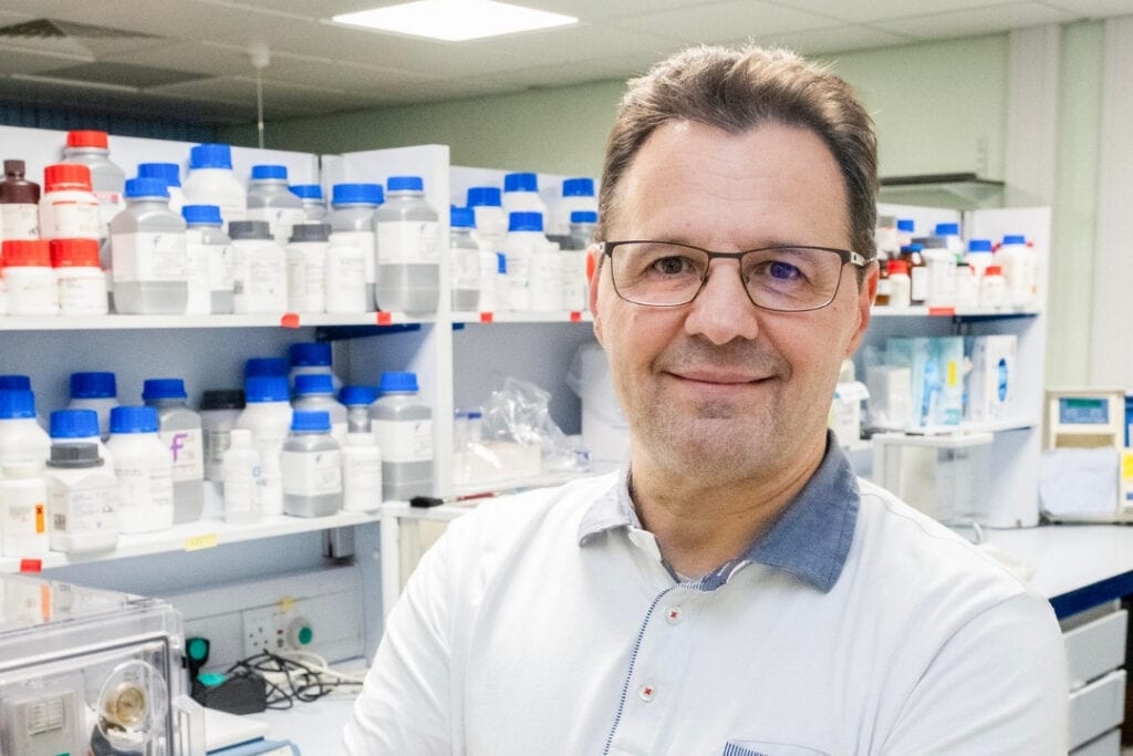 Professor Walter Marcotti wears glasses and stands in a science laboratory.