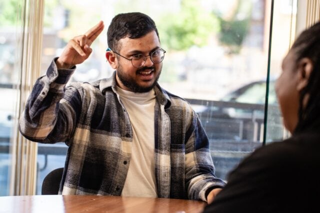 A person sitting at a table signing to the person sitting opposite