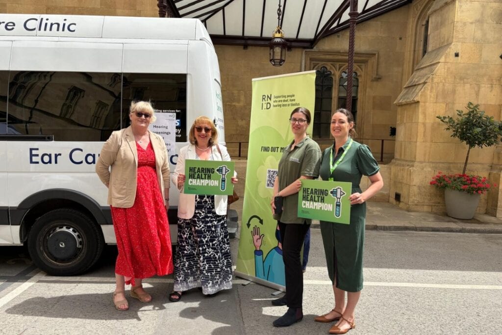 MPs and RNID staff stand beside a mobile hearing health clinic.