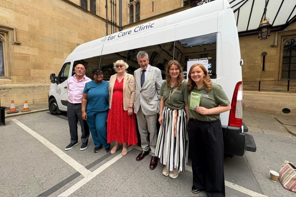 MPs and RNID staff stand beside a mobile hearing health clinic. 