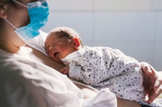 A newborn baby asleep on its parent in a hospital