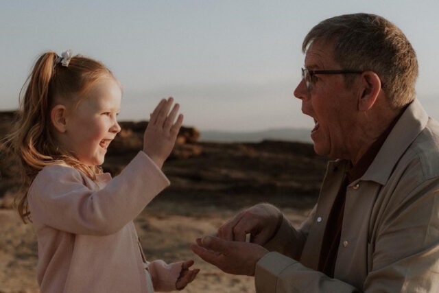 A grandfather and granddaughter signing together on a beach