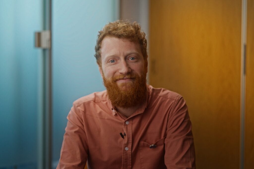 Researcher Chris wears an orange shirt and smiles.