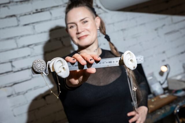 Jenni, Deafmetal founder, holds a display of two ears showcasing Deafmetal jewellery.