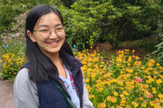 Storyteller Suzie, standing outside in a garden of flowers and smiling